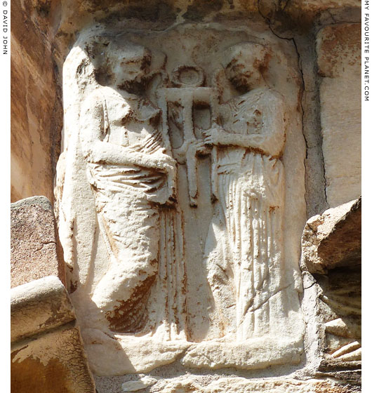 A marble relief of two female figures holding a tripod at My Favourite Planet